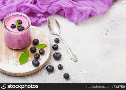 Fresh homemade creamy blueberry yoghurt with fresh blueberries on vintage wooden board and silver spoon on stone table background