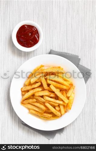 Fresh homemade crispy French fries on plate with a small bowl of ketchup on the side, photographed overhead with natural light