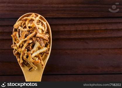 Fresh homemade crispy fried onion strings on wooden spoon, photographed overhead with copy space on the side (Selective Focus, Focus on the top onion strings). Crispy Fried Onion Strings
