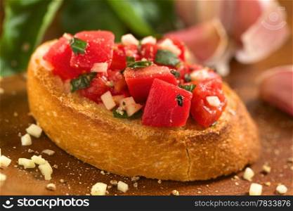 Fresh homemade crispy Italian antipasto called Bruschetta topped with tomato, garlic and basil on wooden board (Selective Focus, Focus on the tomato piece in the front)