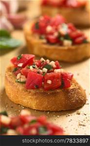 Fresh homemade crispy Italian antipasto called Bruschetta topped with tomato, garlic and basil on wooden board (Selective Focus, Focus on the front of the bruschetta one third into the image)