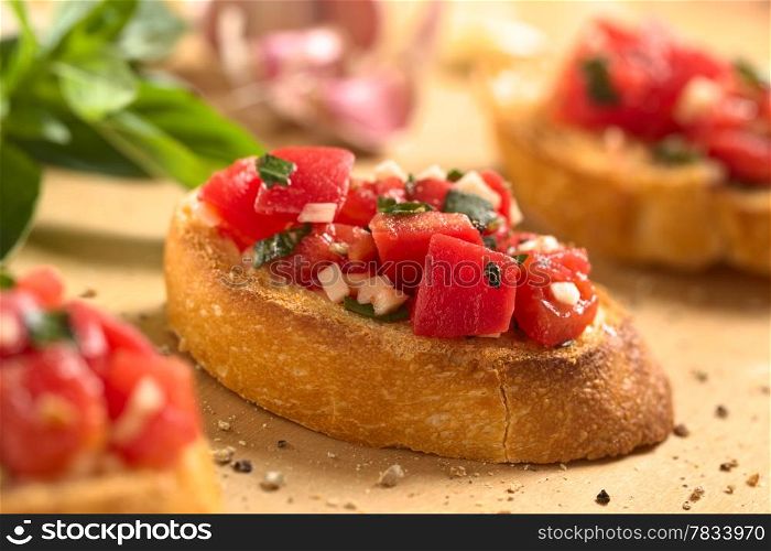 Fresh homemade crispy Italian antipasto called Bruschetta topped with tomato, garlic and basil on wooden board (Selective Focus, Focus on the front of the middle bruschetta)