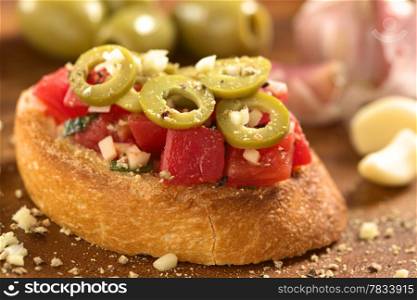 Fresh homemade crispy Italian antipasto called Bruschetta topped with tomato, green olives, garlic and basil on wooden board (Selective Focus, Focus on the front of the bruschetta)