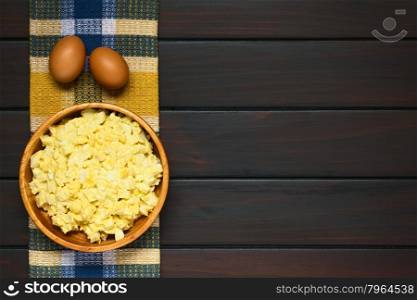 Fresh homemade egg salad prepared with mayonnaise and mustard in wooden bowl, raw eggs above, photographed overhead on dark wood with natural light