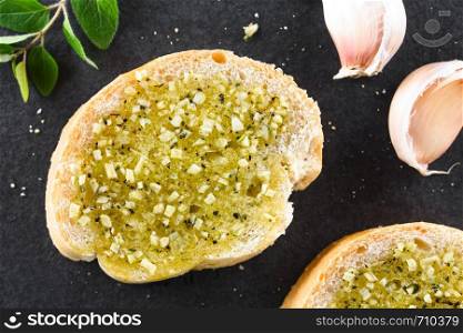 Fresh homemade garlic bread, slices of baguette seasoned with garlic, oregano, salt, pepper and olive oil, photographed overhead on slate (Selective Focus, Focus on the top of the bread). Fresh Garlic Bread