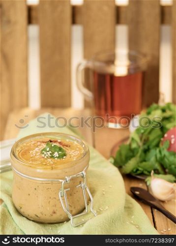 Fresh homemade hummus in a glass jar garnished with sesame seeds, parsley, garlic and olive oil.