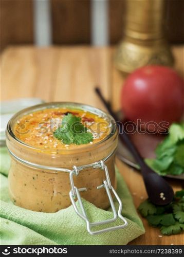 Fresh homemade hummus in a glass jar garnished with sesame seeds, parsley, garlic and olive oil.