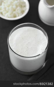 Fresh homemade kefir drink in glass, kefir grains and milk in the back, photographed with natural light (Selective Focus, Focus one third into the kefir drink) (Digitally Altered: Desaturated Image). Kefir Drink