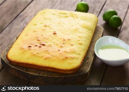 Fresh homemade key lime cake on wooden board with lime icing on the side and key limes in the back (Selective Focus, Focus one third into the cake)