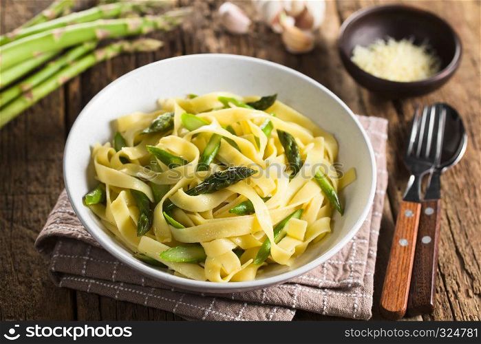 Fresh homemade pasta dish of fettuccine or tagliatelle, green asparagus, garlic and lemon juice in bowl, ingredients and grated cheese in the back (Selective Focus, Focus on the asparagus head in the middle). Fettuccine with Green Asparagus, Garlic and Lemon