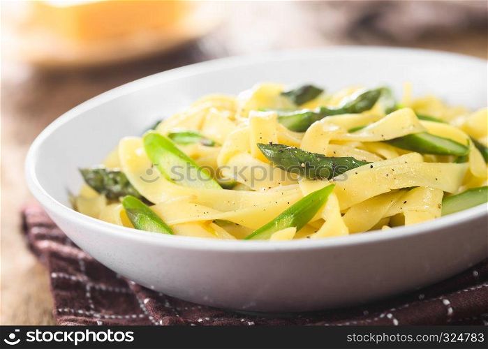 Fresh homemade pasta dish of fettuccine or tagliatelle, green asparagus, garlic and lemon juice in bowl, ground black pepper on the top (Selective Focus, Focus one third into the dish). Fettuccine with Green Asparagus, Garlic and Lemon