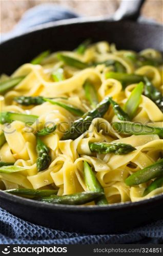Fresh homemade pasta dish of fettuccine or tagliatelle, green asparagus, garlic and lemon juice in cast iron skillet (Selective Focus, Focus one third into the frying pan). Fettuccine with Green Asparagus, Garlic and Lemon
