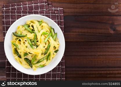 Fresh homemade pasta dish of fettuccine or tagliatelle, green asparagus, garlic and lemon juice in bowl, ground black pepper on the top, photographed overhead with copy space on the right side. Fettuccine with Green Asparagus, Garlic and Lemon