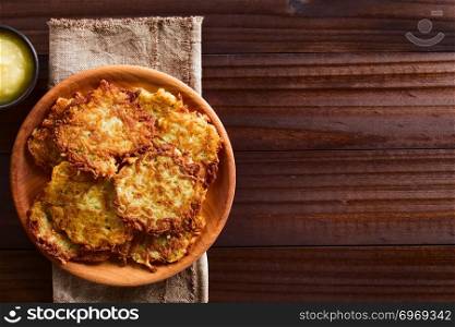 Fresh homemade potato fritters or pancakes on wooden plate with apple sauce on the side, a traditional German snack or dish called Kartoffelpuffer or Reibekuchen, photographed overhead on dark wood with copy space on the side. Fresh Homemade Potato Fritters or Pancakes