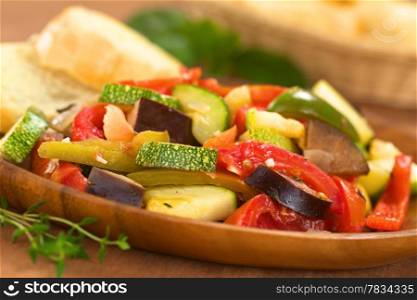 Fresh homemade Ratatouille made of eggplant, zucchini, bell pepper and tomato and seasoned with herbs (garlic, thyme, oregano) on wooden plate with baguette in the back (Selective Focus, Focus one third into the meal). Ratatouille