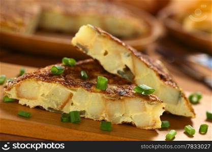 Fresh homemade Spanish tortilla (omelette with potatoes and onions) slices with scallion on top on wooden cutting board (Selective Focus, Focus on the front upper edge of the lower tortilla slice)