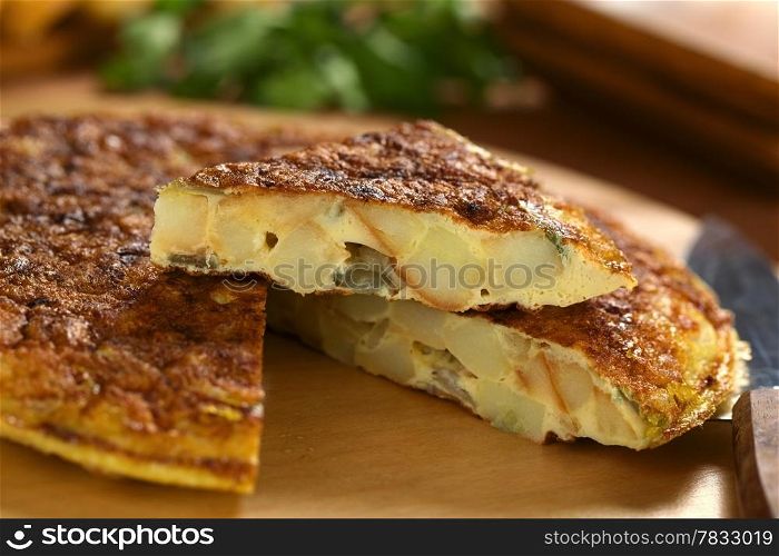 Fresh homemade Spanish tortilla (omelette with potatoes and onions) with a slice on top (Selective Focus, Focus on the front of the tortilla slice on top)