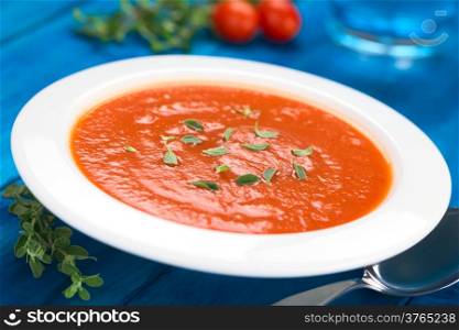 Fresh homemade tomato soup with oregano leaves on top served in soup plate on blue wood (Selective Focus, Focus one third into the soup)