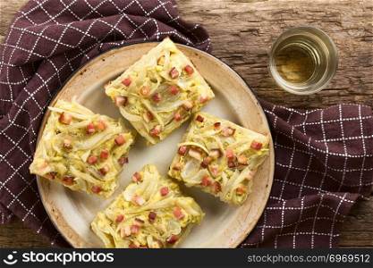 Fresh homemade traditional German Zwiebelkuchen onion cake, a savory baked pastry or pie made of yeast dough topped with onion, bacon, eggs and cream, glass of white wine on the side, photographed overhead. German Zwiebelkuchen Onion Cake