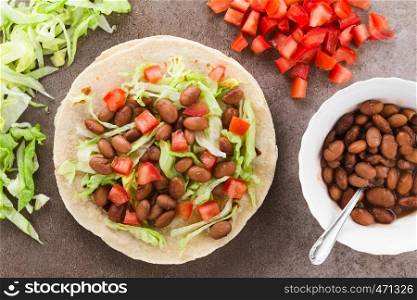Fresh homemade vegan tacos made of flour tortilla with lettuce, cooked beans and tomatoes, photographed overhead. Flour Tortilla with Beans, Lettuce and Tomato
