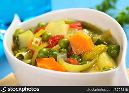 Fresh homemade vegetable soup made of carrot, leek, pea, potato, onion and tomato (Selective Focus, Focus on the carrot in the middle of the soup)