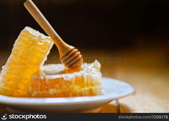 Fresh honey healthy food yellow sweet honeycomb slice with wooden dipper on white plate and dark background