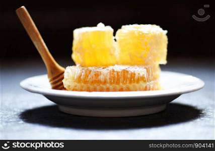 Fresh honey healthy food yellow sweet honeycomb slice with wooden dipper on white plate and dark background