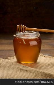 fresh honey in a transparent glass jar and a wooden spoon on a brown table