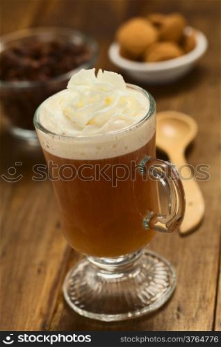 Fresh hot chocolate herbal tea made of cacao shell flakes, which is rich in flavonoids and antioxidants, served in glass with whipped cream on top on dark wood (Selective Focus, Focus on the front of the cream)