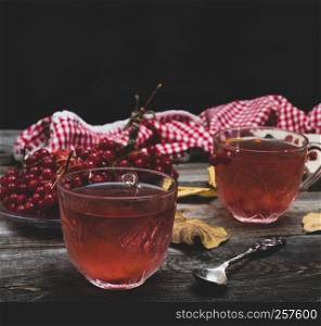 Fresh hot tea from viburnum berries in a transparent glass cup on a gray wooden background
