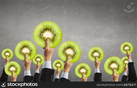 Fresh idea. Group of business people holding kiwi slice in raised hands