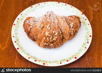fresh italian croissant filled by nuts and chocolate cream on wooden table