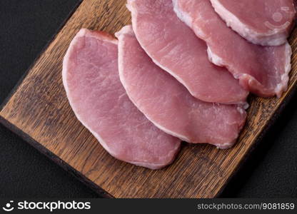 Fresh juicy pork on a wooden cutting board with spices and salt on a dark concrete background