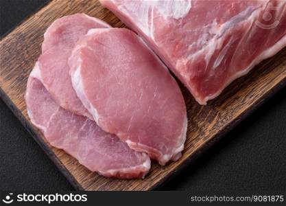 Fresh juicy pork on a wooden cutting board with spices and salt on a dark concrete background