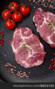 Fresh juicy pork steaks with salt, spices and herbs on a dark concrete background