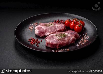 Fresh juicy pork steaks with salt, spices and herbs on a dark concrete background
