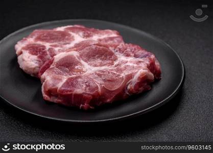 Fresh juicy pork steaks with salt, spices and herbs on a dark concrete background