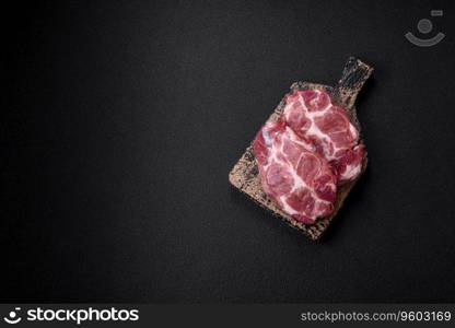 Fresh juicy pork steaks with salt, spices and herbs on a dark concrete background