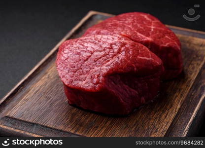 Fresh juicy raw beef medallions with salt and spices on a dark concrete background