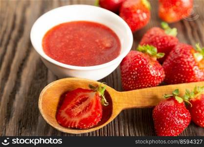 Fresh juicy ripe red strawberry and strawberry jam on a brown wooden background