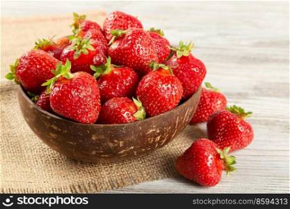 Fresh juicy ripe red strawberry in a brown coconut plate on a wooden background