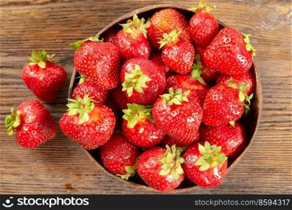 Fresh juicy ripe red strawberry in a coconut plate on a brown wooden background. Top view