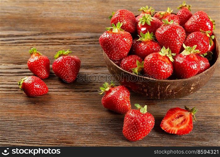 Fresh juicy ripe red strawberry in a coconut plate on a brown wooden background