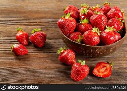 Fresh juicy ripe red strawberry in a coconut plate on a brown wooden background