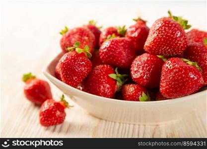 Fresh juicy ripe red strawberry in a white plate on a wooden background