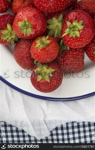 Fresh juicy strawberries on vintage enamelware on rustic background