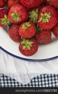 Fresh juicy strawberries on vintage enamelware on rustic background