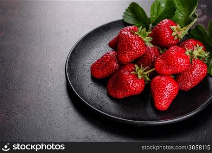 Fresh juicy strawberries with leaves. Fresh summer crop of strawberry berries. Beautiful juicy fresh strawberries on the concrete surface of the table