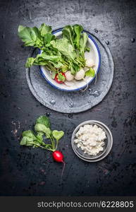 Fresh juicy white and red radishes with leaves and grain fresh cheese on dark rustic background , top view