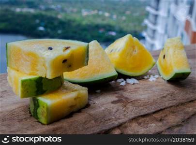 Fresh juicy yellow watermelon cut into triangles on old wooden table at balcony with city view. Tropical fruits. Copy space, Select focus.